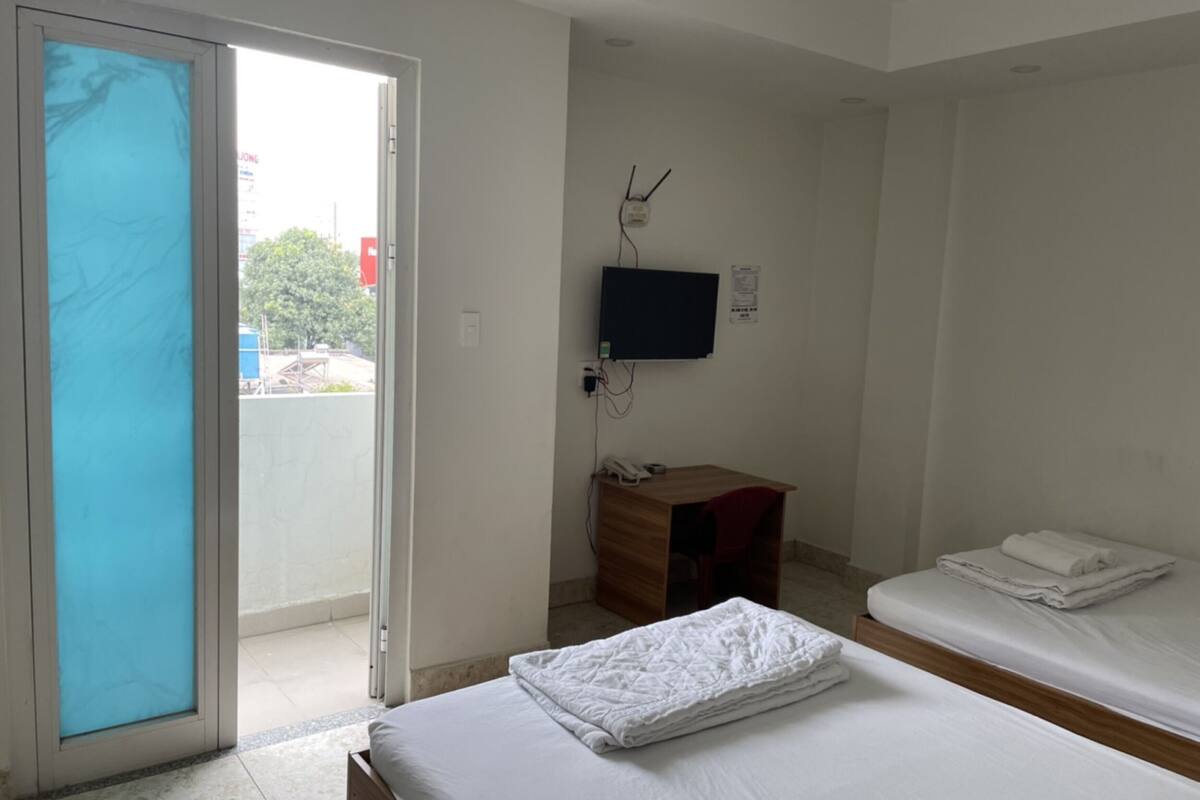 A hotel room with a bed, a desk, a TV, and a sliding glass door leading to an outdoor area.