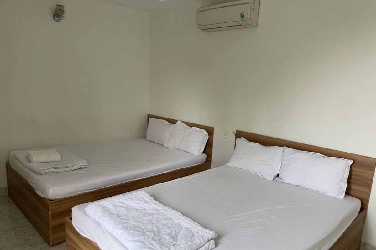 Two single beds with wooden headboards and white bedding, a wall-mounted air conditioner, and a small decorative item on the wall.