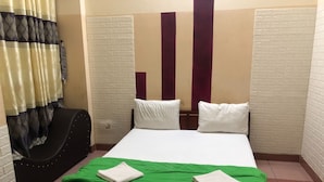 Una habitación de hotel con una cama, colcha verde, almohadas blancas, una silla negra y una cortina.