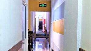 A hotel hallway with a clear exit sign, a staircase, and a door leading to another room.