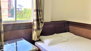 A hotel room with a bed, a small table, and a window with curtains.