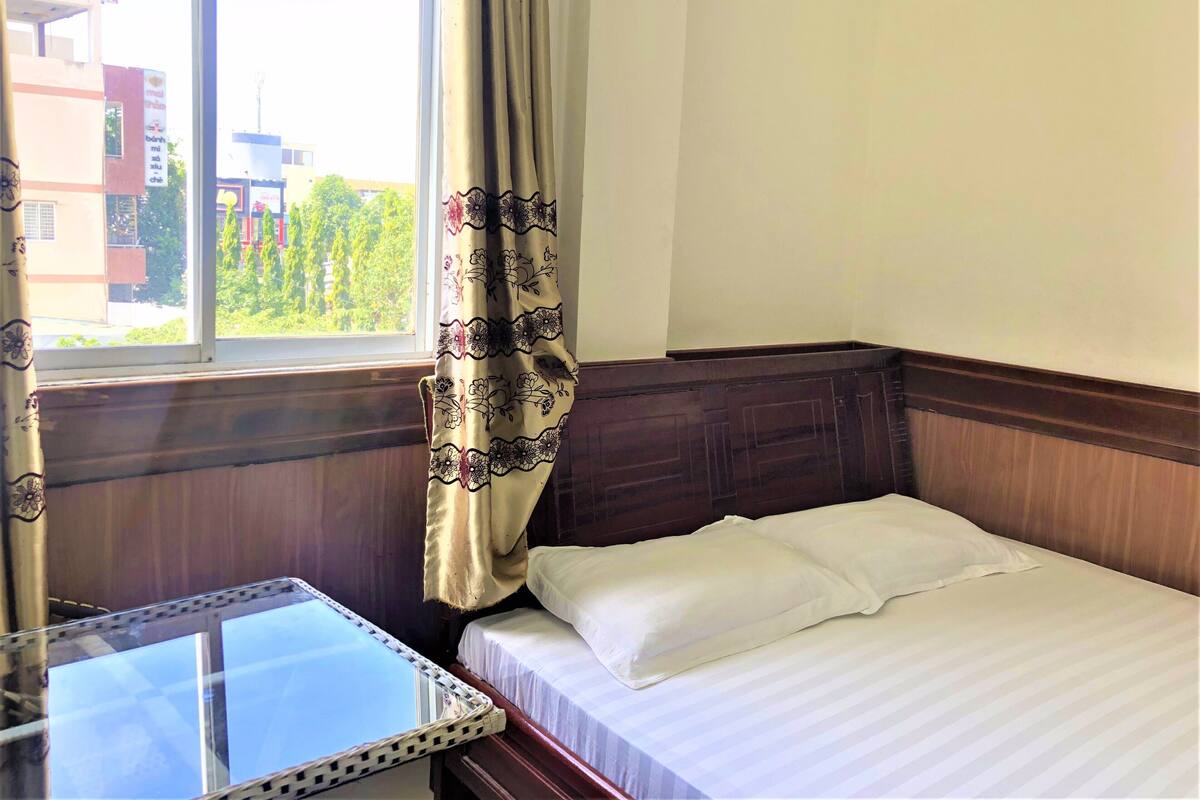 Una habitación de hotel con cama, una mesita y una ventana con cortinas.