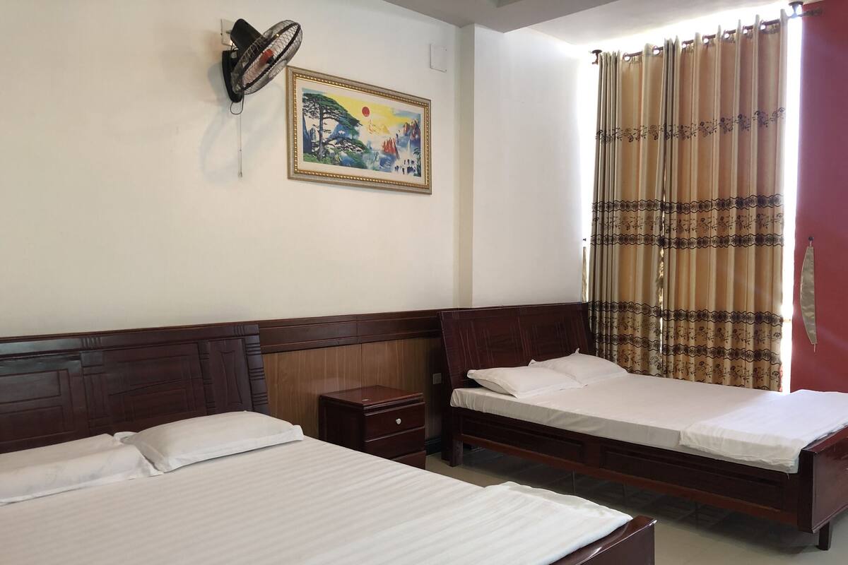 Una habitación de hotel con dos camas, una mesita de noche, un ventilador de pared y un cuadro.