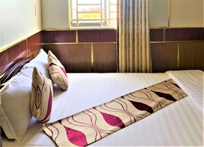 A hotel room with a bed, pillows, a bedside table, a window with curtains, and a wall with a wooden panel design. - Hong Dao 2 Hotel (Can Tho)