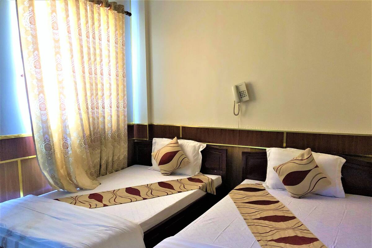 A hotel room with two single beds, a telephone, and a window with curtains.