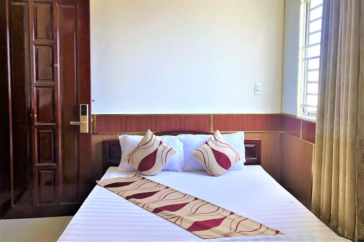 A hotel room with a large bed, wooden paneling on the walls, and a window with curtains.
