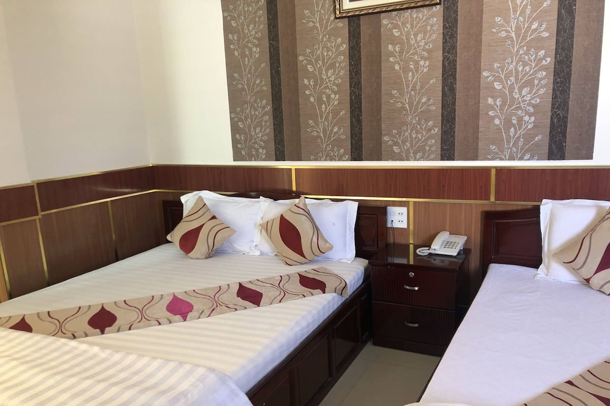 A hotel room with two beds, a bedside table with a phone, and a wall-mounted mirror.