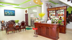 A reception area with a wooden desk, a red stool, and a counter displaying various items. - Thanh Tung Hotel (Can Tho)