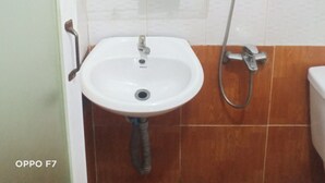 Een badkamer met een wit wastafelmeubel, een glazen plank, een handdouche en een spiegel.