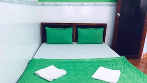 Een bed met groen beddengoed en twee kussens, een houten hoofdbord en een deur aan de rechterkant.