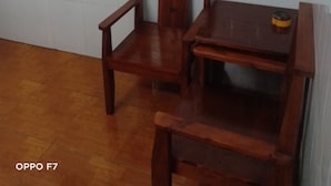 Een kamer met een houten stoel en tafel, een wandtelevisie en een betegelde vloer.