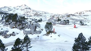 Eine verschneite Berglandschaft mit felsigen Vorsprüngen und vereinzelten Bäumen.