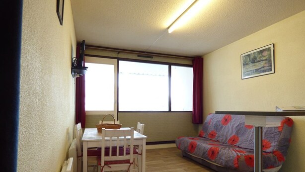 Ein Zimmer mit Esstisch und Stühlen, einer Couch, einem Fenster mit Vorhängen und einem gerahmten Bild an der Wand.