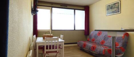A room with a dining table and chairs, a sofa, a window with curtains, and a framed picture on the wall.