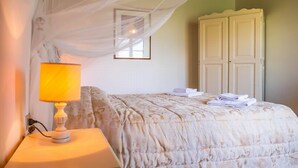 Ein ordentlich bezogenes Bett mit floralem Überwurf, eine Nachttischlampe und ein Schrank an einer grünen Wand.