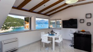 A modern kitchen with a dining area, large windows with a view of the sea, and a black countertop with a bowl of fruit. - Apartment Mali Skoj (Dubrovnik)