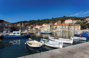 Um porto com barcos atracados, edifícios de pedra com telhados vermelhos e um horizonte montanhoso.