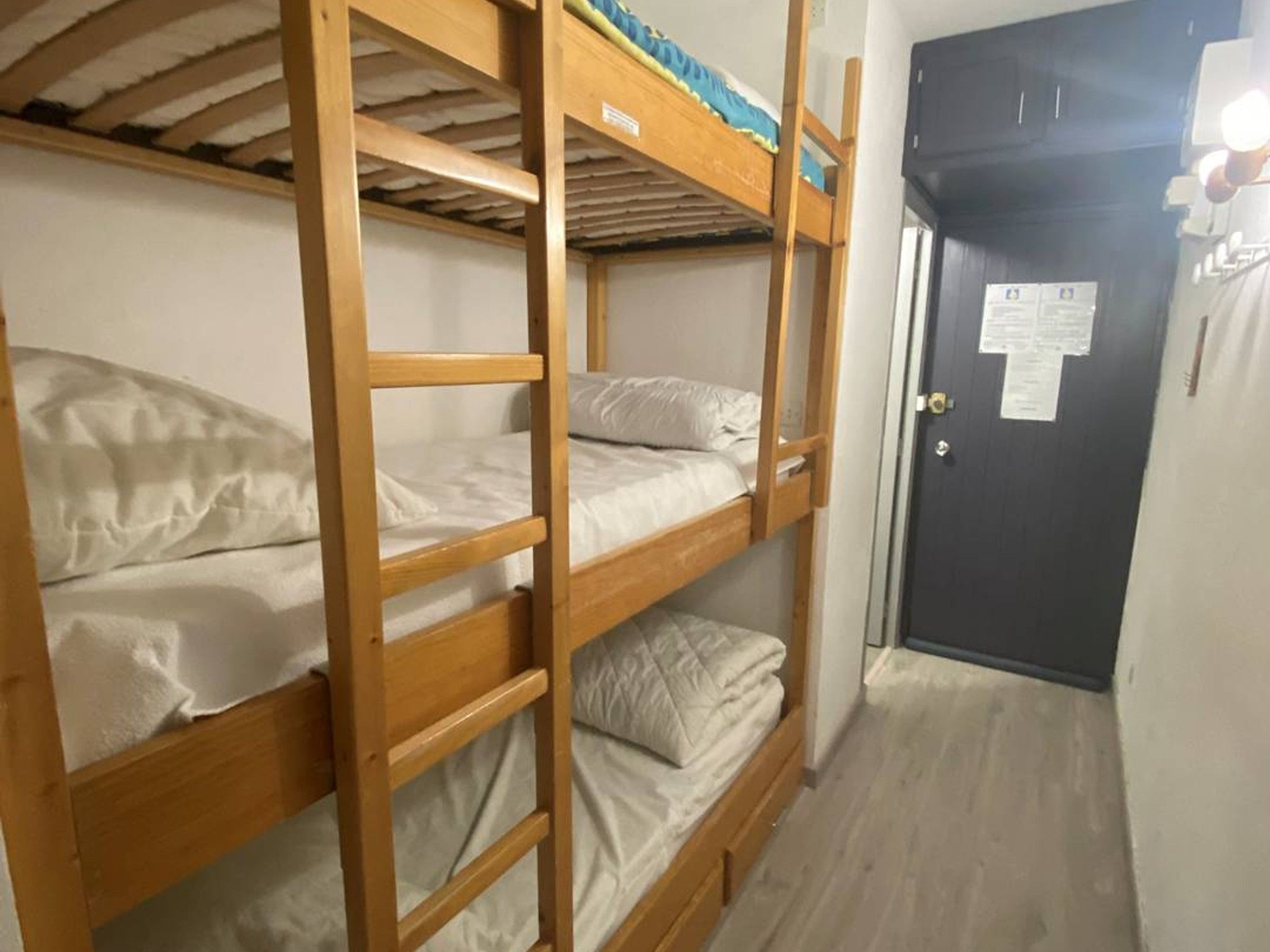 Una habitación con literas, una puerta con un aviso y suelo de madera.