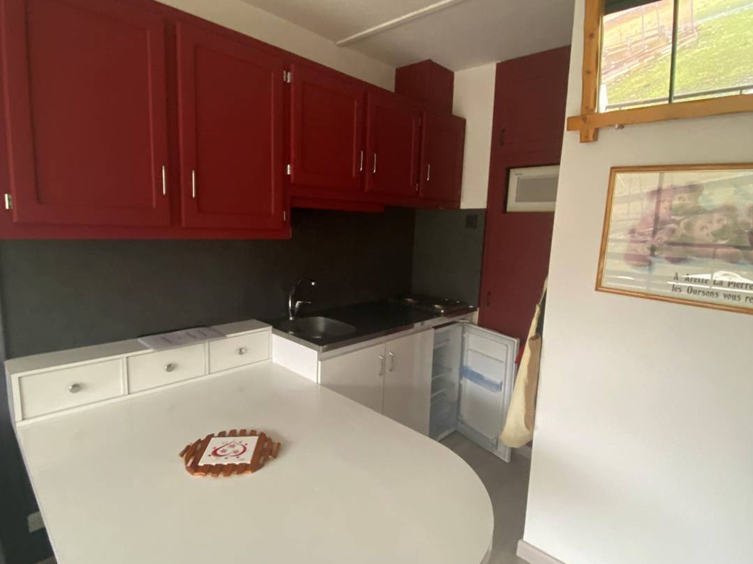 A kitchen with red cabinets, a white countertop, and a framed picture on the wall.