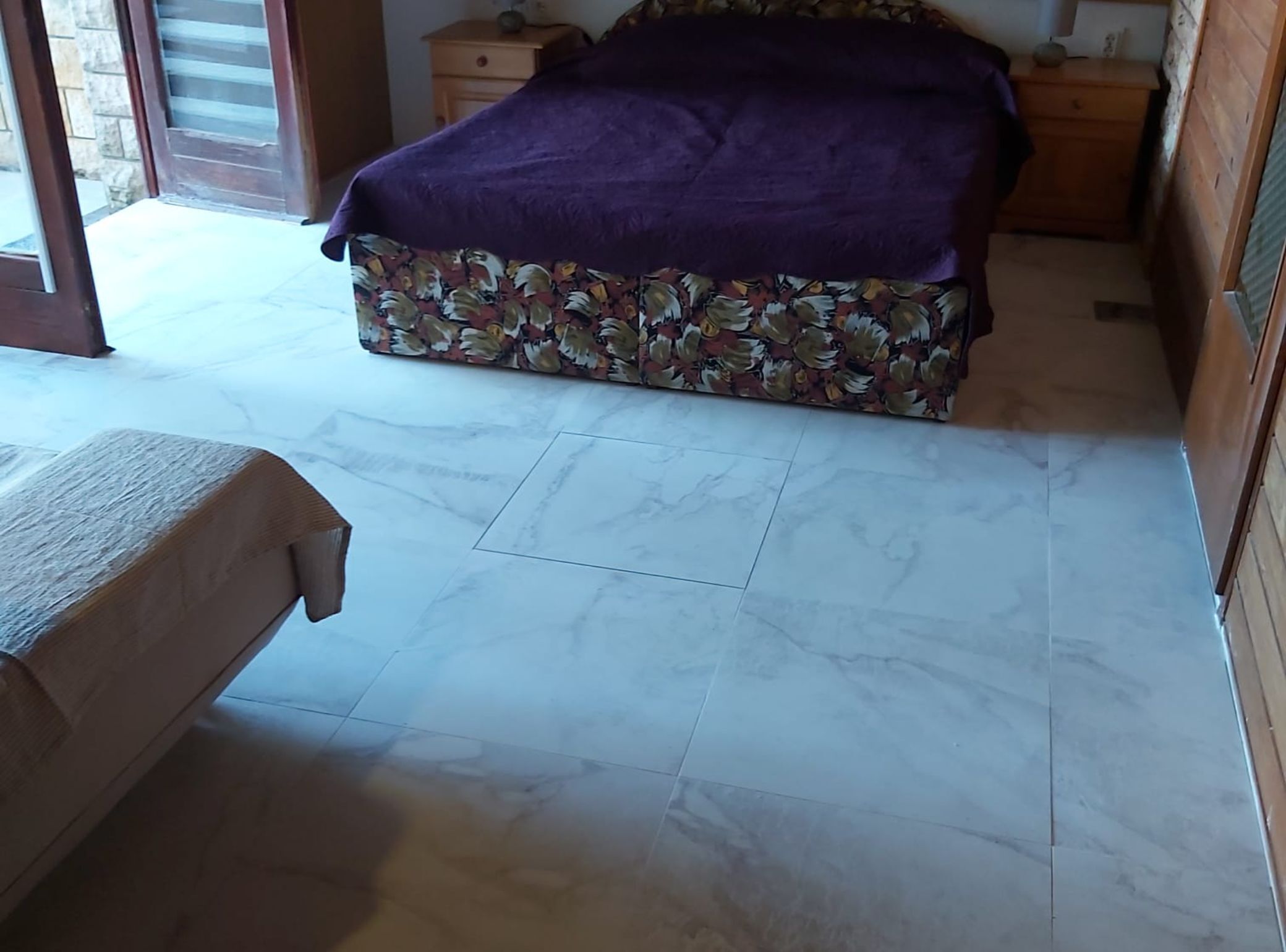 A bedroom with a bed, a wooden bench, and a marble floor.