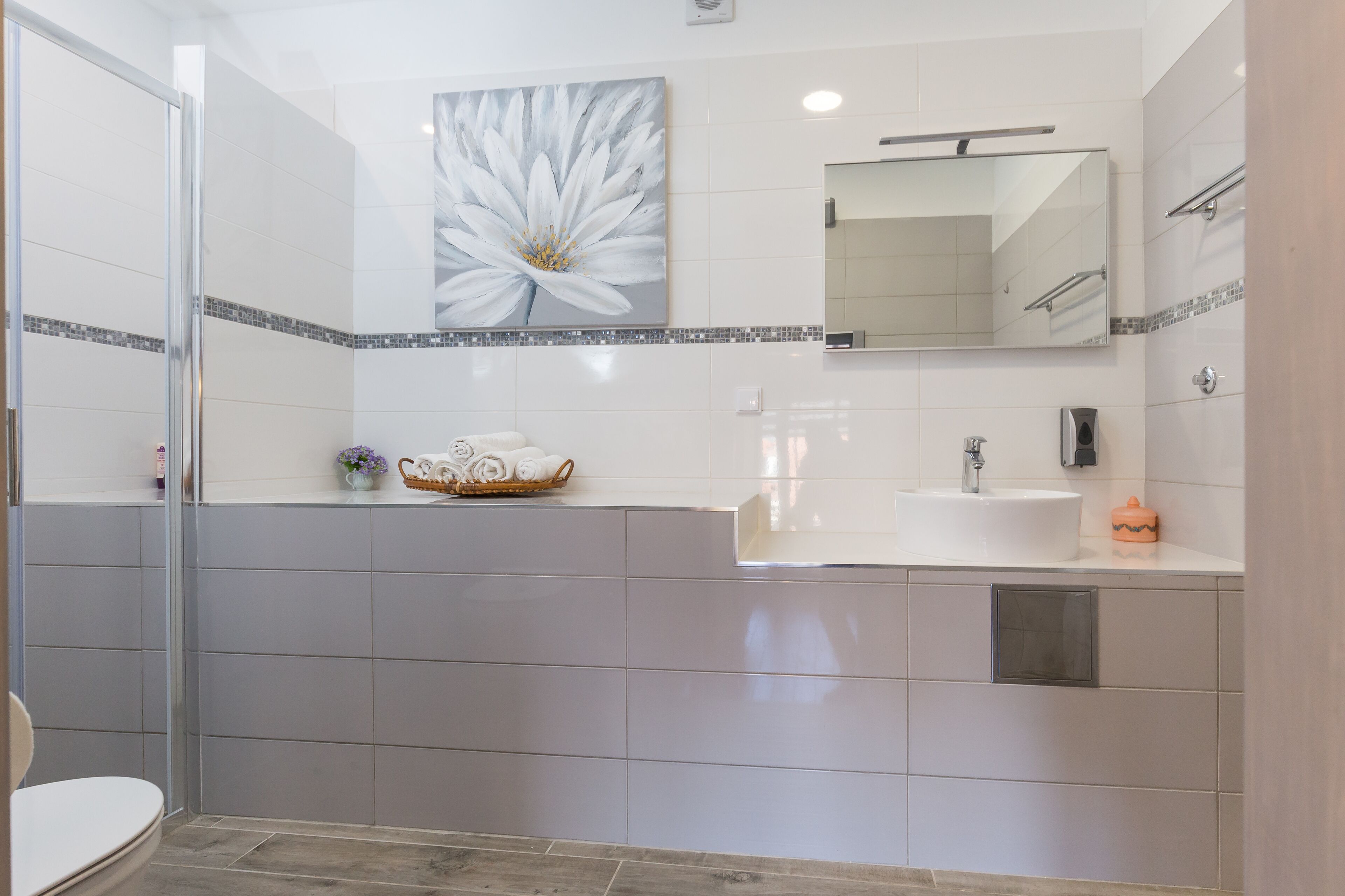 A modern bathroom with a glass shower enclosure, a large mirror, and a white sink with a tiled backsplash.