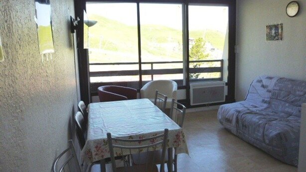 A room with a dining table, chairs, a sofa, and a large window with a view of hills. - Family studio for 6, ski-in/out, balcony, free parking, ski locker (Arette)