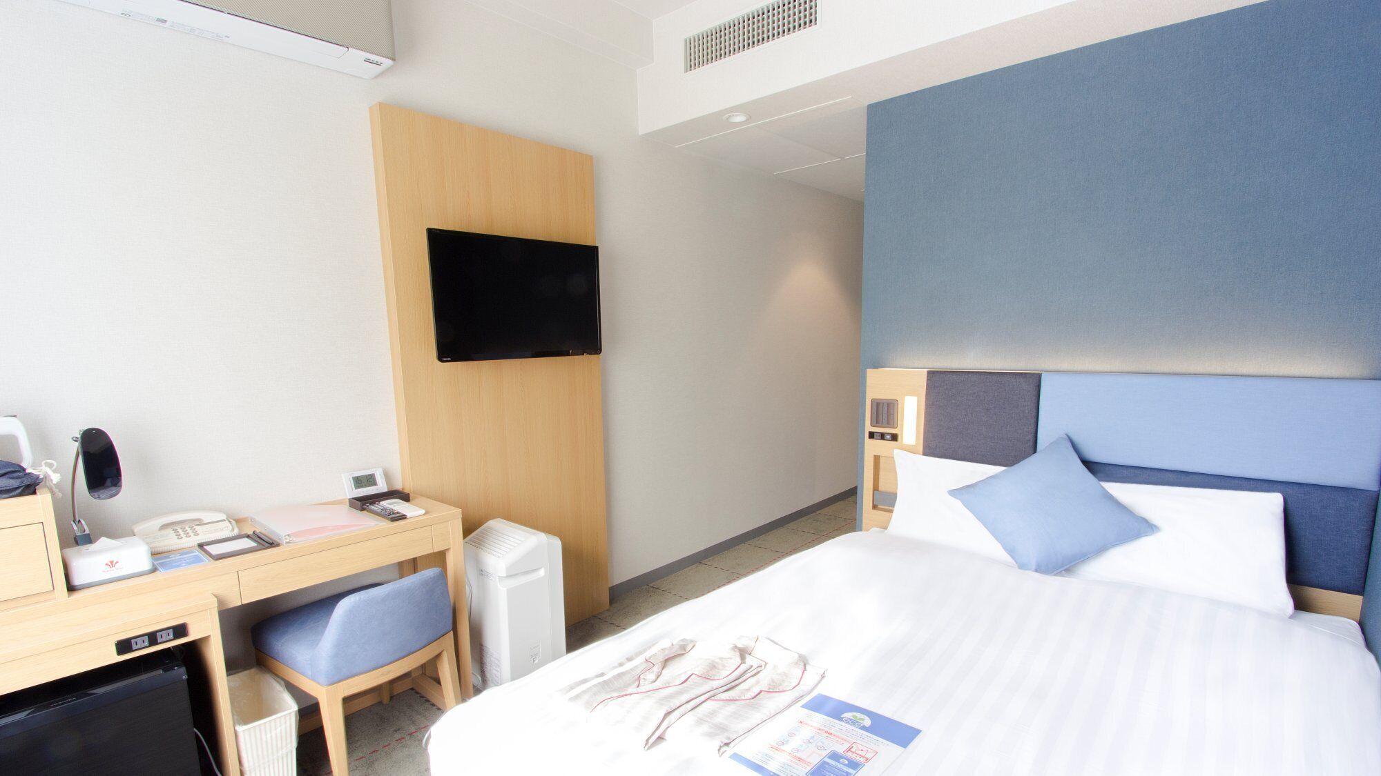 Ein Hotelzimmer mit Bett, Schreibtisch, Stuhl, Fernseher und einem kleinen Schreibtisch mit Telefon und Lampe.