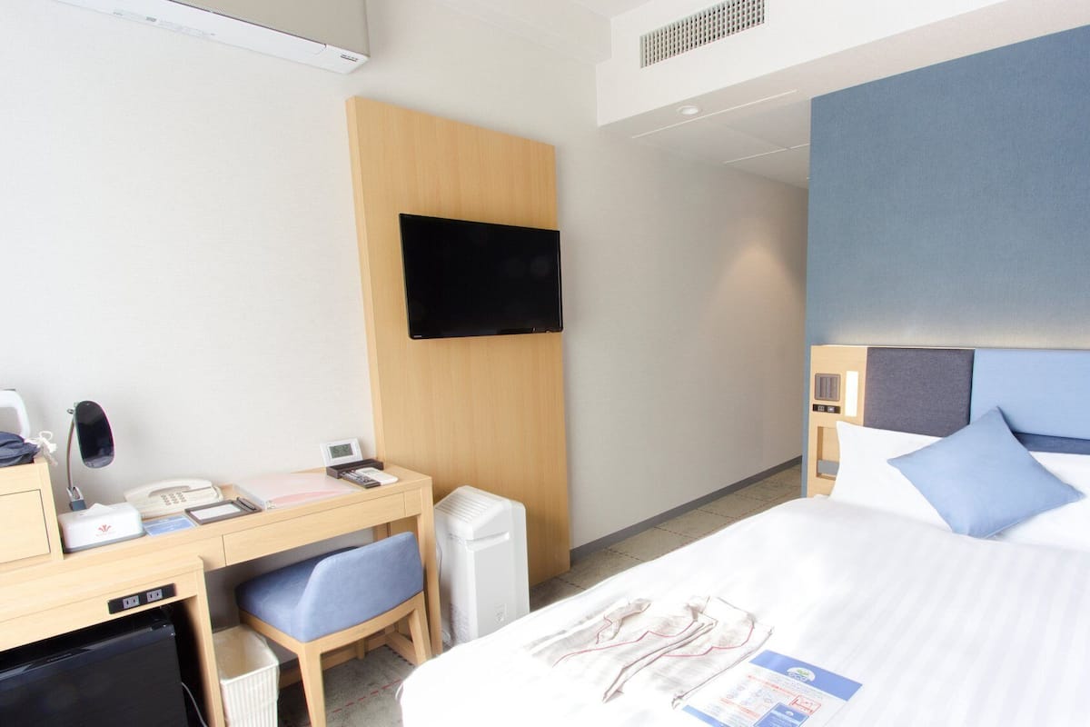 Ein Hotelzimmer mit Bett, Schreibtisch, Stuhl, Fernseher und einem kleinen Schreibtisch mit Telefon und Lampe.