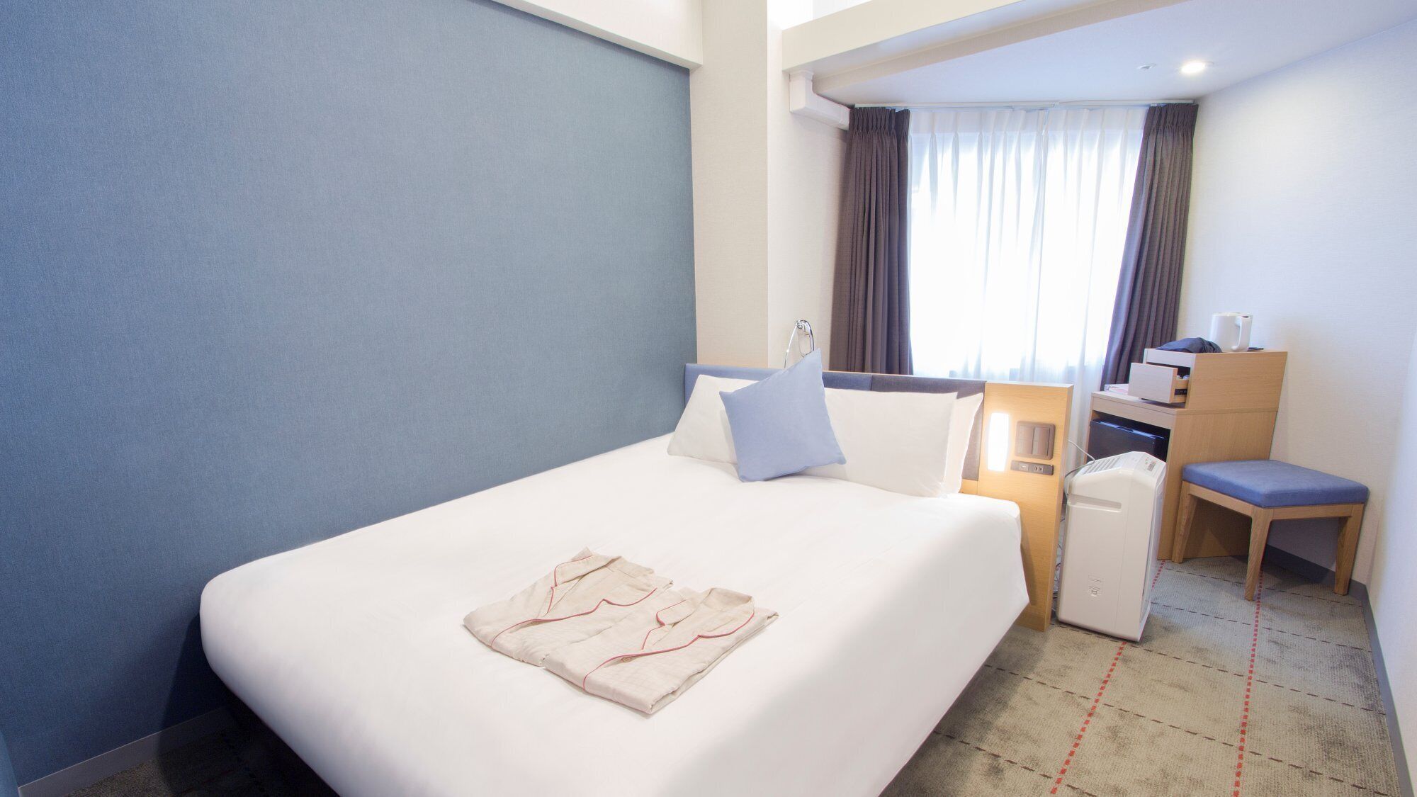 Ein Hotelzimmer mit Bett, Schreibtisch, Stuhl und einem Vorhangfenster.