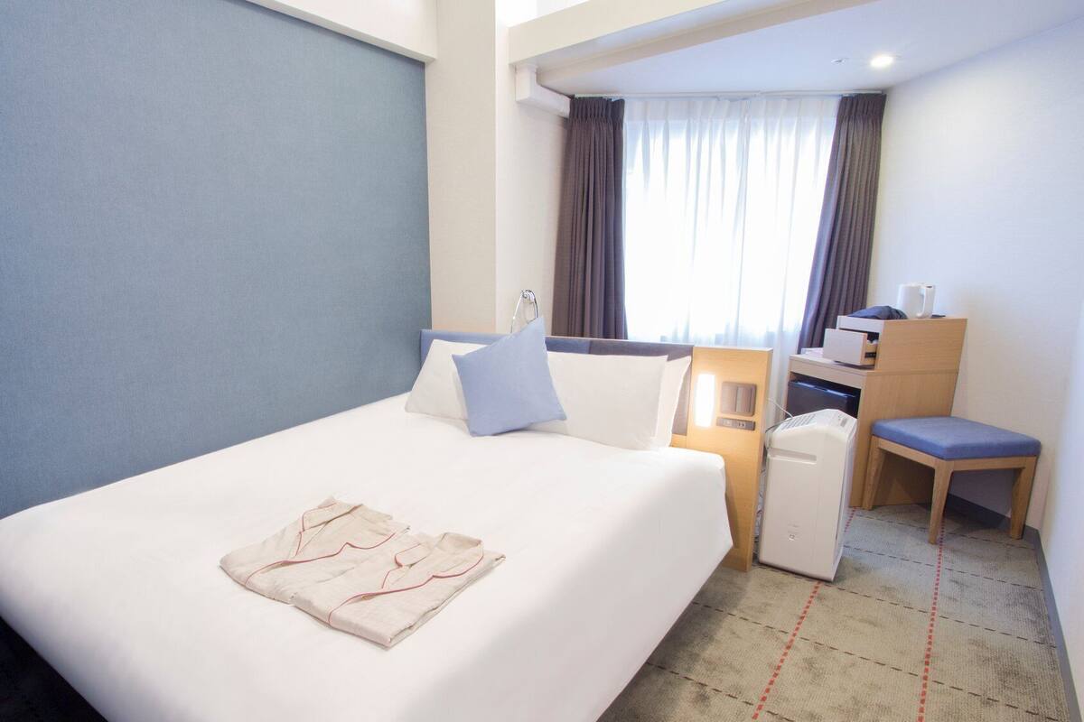 Ein Hotelzimmer mit Bett, Schreibtisch, Stuhl und einem Vorhangfenster.