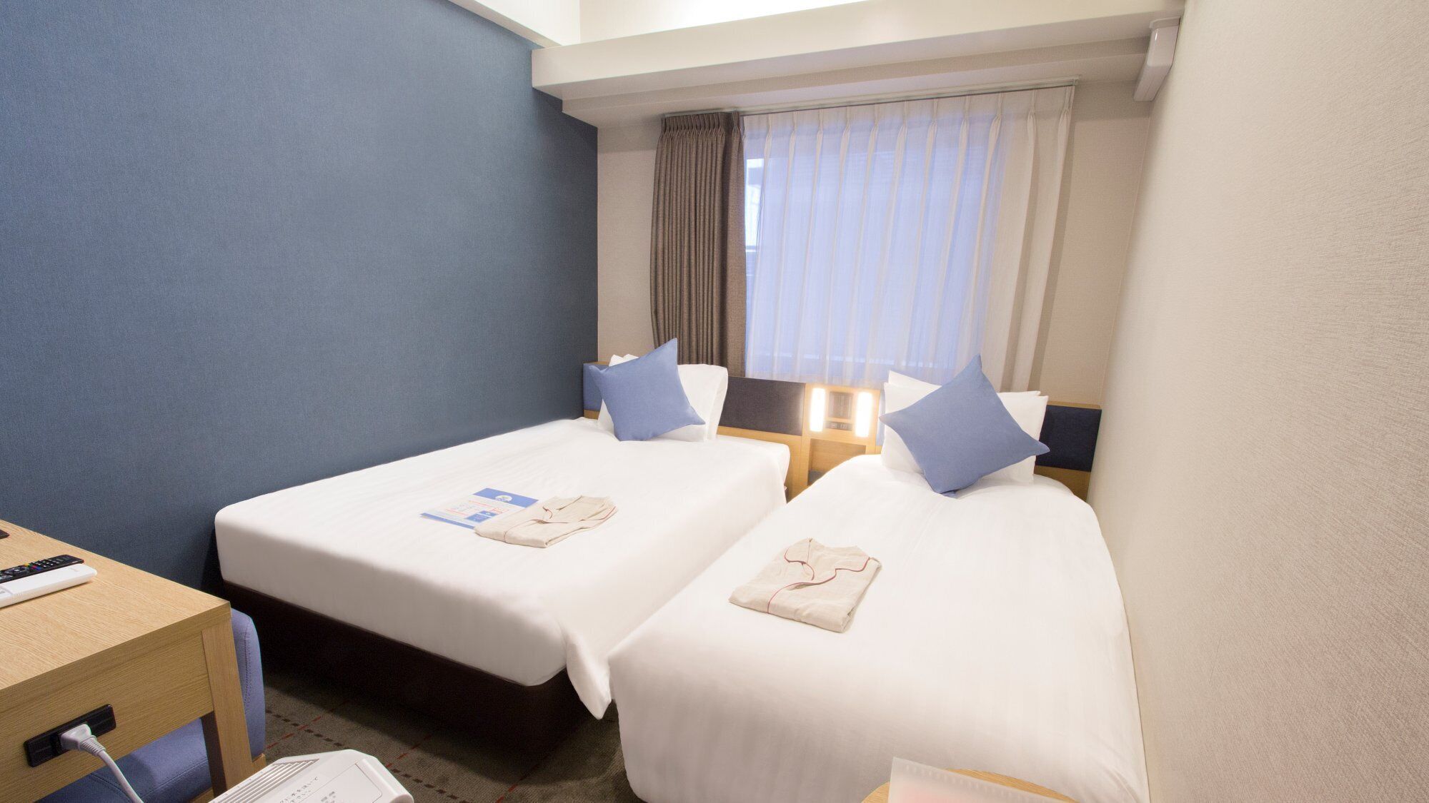 Ein Hotelzimmer mit zwei Betten, einem Schreibtisch und einem Fenster mit Vorhängen.