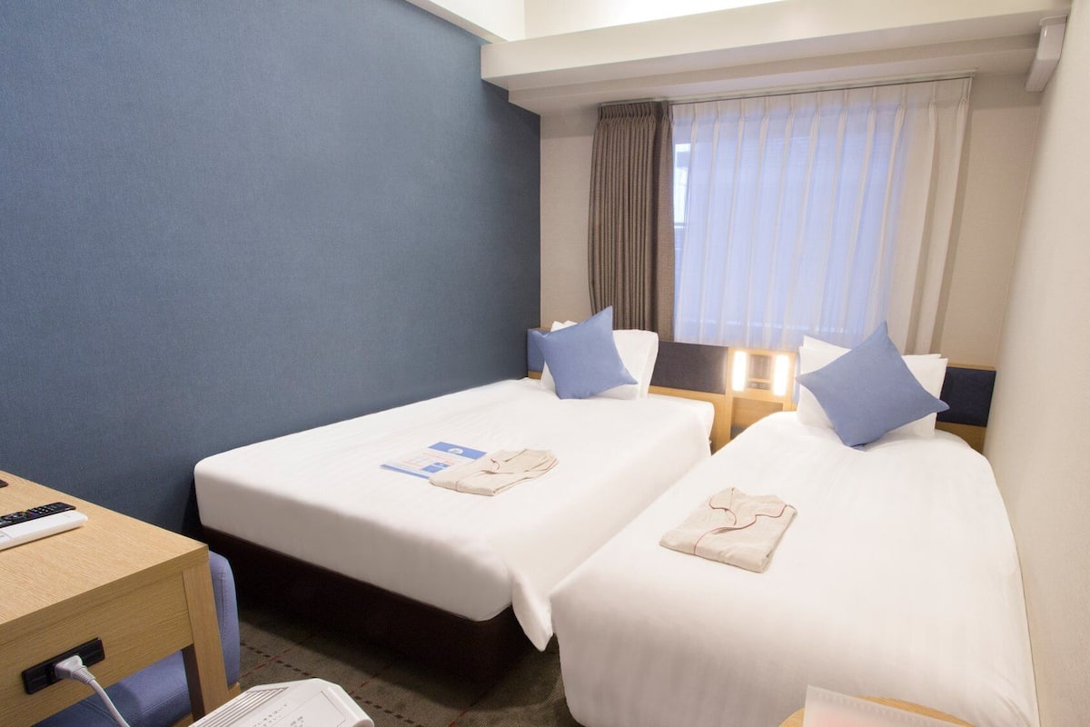 Ein Hotelzimmer mit zwei Betten, einem Schreibtisch und einem Fenster mit Vorhängen.
