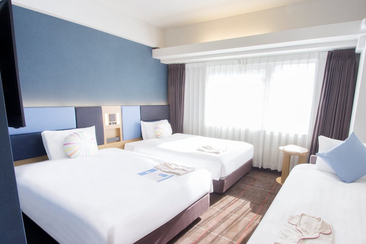 Ein Hotelzimmer mit zwei Betten, einem Fernseher, einem kleinen Tisch und einem Fenster mit Vorhängen.
