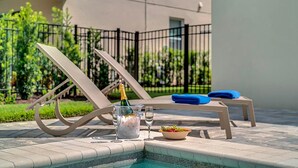 A poolside area with lounge chairs, a table with a bottle of champagne, a glass of water, and a bowl of fruit. - Rent this Luxury 5 Star Villa on Encore Resort at Reunion, Orlando Villa 4434 (Orlando)