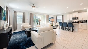 A modern living room with a white sofa, a coffee table, and a TV on a stand. There is a kitchen area with a microwave, stove, and bar stools. - Rent this Luxury 5 Star Villa on Encore Resort at Reunion, Orlando Villa 4434 (Orlando)