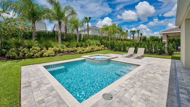 A rectangular swimming pool with a hot tub, surrounded by a paved deck and a grassy area with palm trees and shrubs. - Rent this Luxury 5 Star Villa on Encore Resort at Reunion, Orlando Villa 4434 (Orlando)