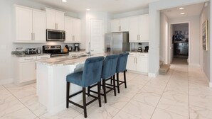 A modern kitchen with white cabinetry, a central island with bar stools, stainless steel appliances, and a marble floor. - Rent this Luxury 5 Star Villa on Encore Resort at Reunion, Orlando Villa 4434 (Orlando)