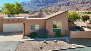 A single-story building with a tiled roof, a garage, and a small patio area with a view of a mountainous landscape. - Coyote Run @ Rim Village - Pet Friendly (Moab)