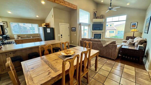 A spacious kitchen with a wooden dining table, a built-in island, and a cozy living area with a sofa and a fireplace. - Coyote Run @ Rim Village - Pet Friendly (Moab)