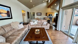 A spacious living area with a large sofa set, a wooden coffee table, and a kitchen in the background. - Coyote Run @ Rim Village - Pet Friendly (Moab)