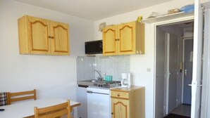 Een kleine keuken met houten kastjes, een wit aanrecht, een magnetron, een spoelbak en een koffiezetapparaat.