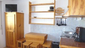 Een kleine keuken met houten kastjes, een inbouwplankje en een eethoek met krukken.