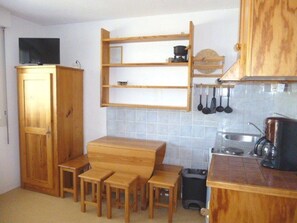 A compact kitchen with wooden cabinets, a built-in shelf, and a small dining area with stools. - Studio at the foot of the slopes - 4 pers, Parking, Elevator (Arette)