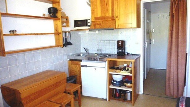 Een kleine keuken met houten kastjes, een magnetron, een koffiezetapparaat en een eethoekje met een houten tafel en stoelen.