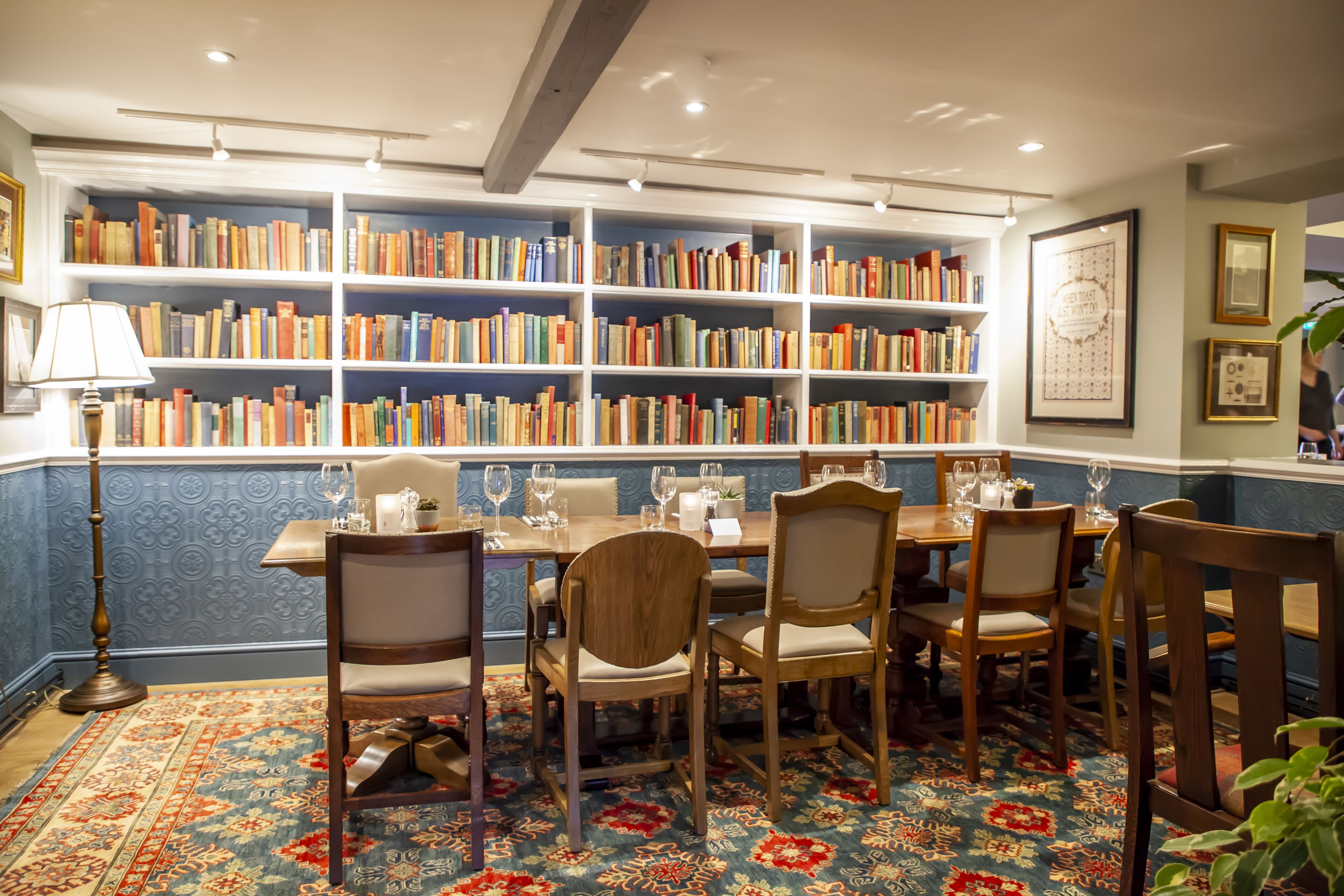 Een bibliotheek met boekenkasten, een eettafel met stoelen en een kamerbreed tapijt met patroon.