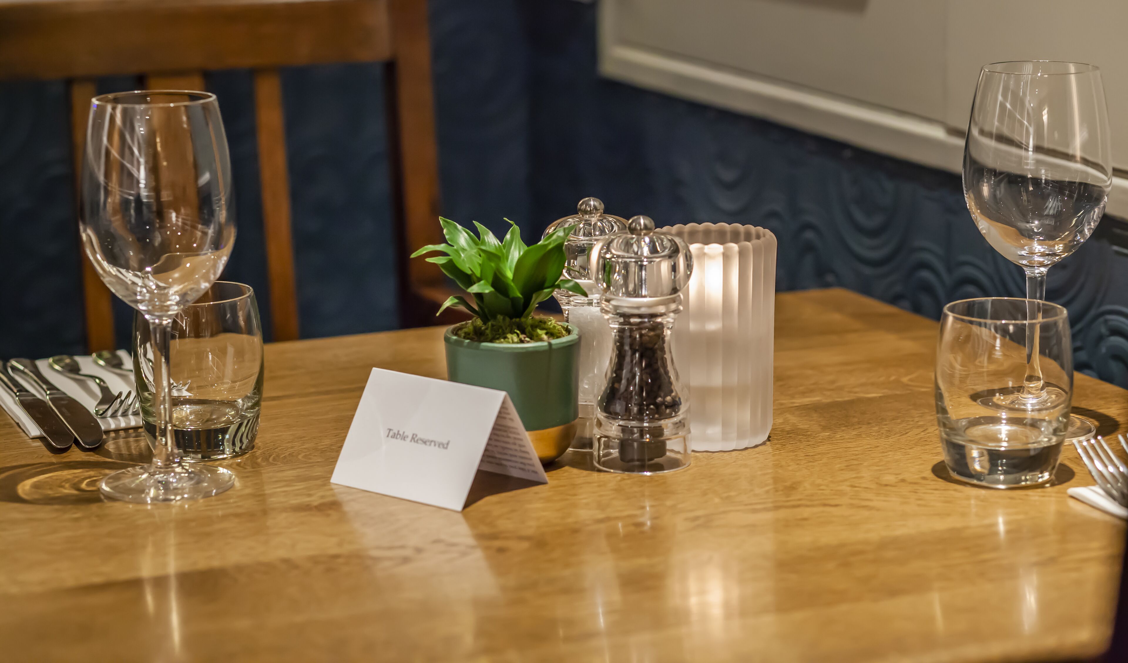 A table set with wine glasses, a menu, a plant, salt and pepper shakers, and a candle.