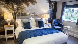 Un lit bien fait, recouvert d’une couette bleue, deux tables de chevet avec des lampes, une chaise et une fenêtre avec des rideaux.