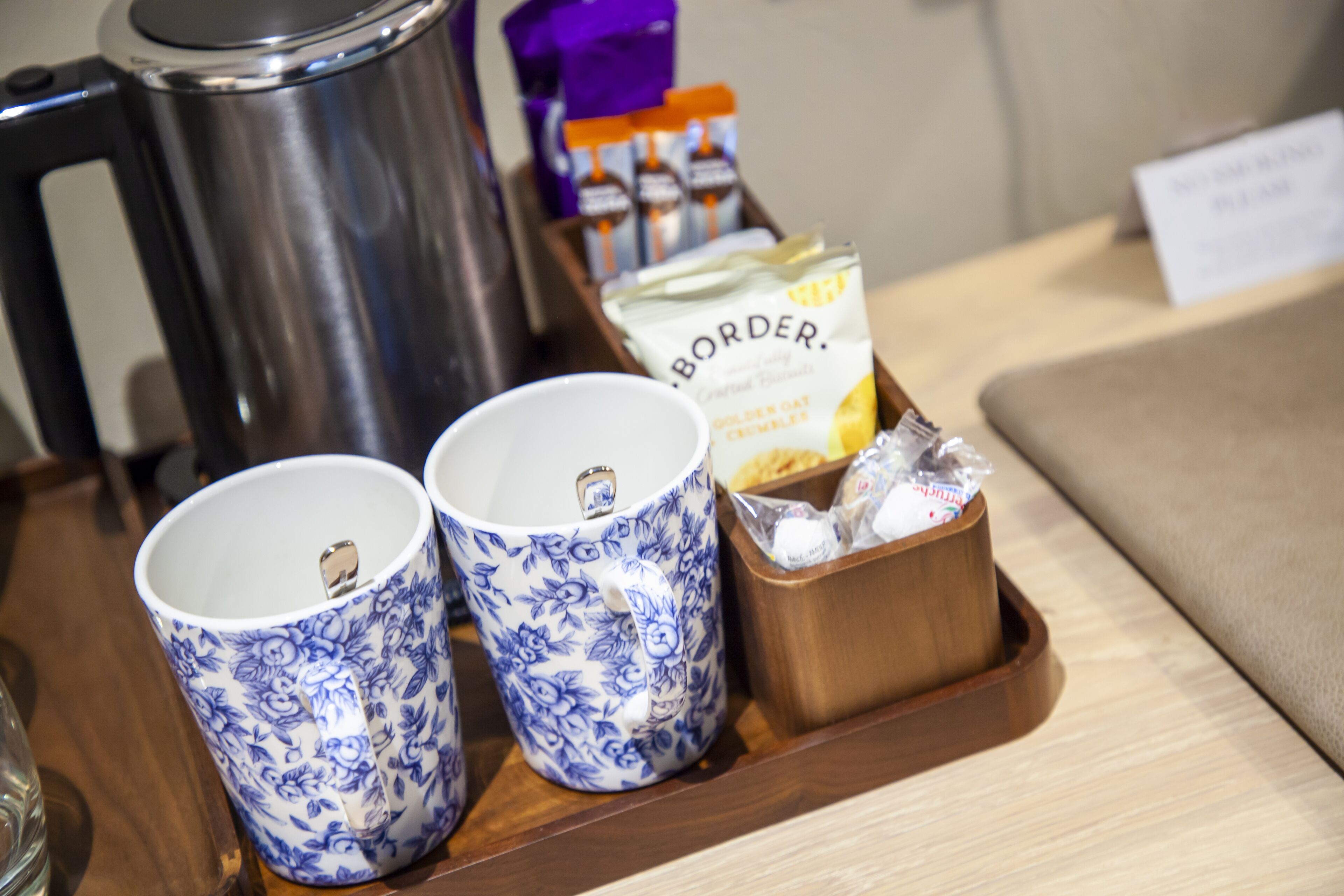 Een dienblad met twee mokken met bloemenprint, een koffiepot en een doosje snacks.