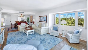 A spacious living room with a large window, a dining area, and a cozy seating arrangement. - LIGHTHOUSE A311 - Gorgeous views from top floor Sanibel condo (Sanibel)