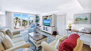 A spacious living room with a large TV, comfortable seating, a balcony with a view, and a neatly organized entertainment unit. - LIGHTHOUSE A311 - Gorgeous views from top floor Sanibel condo (Sanibel)